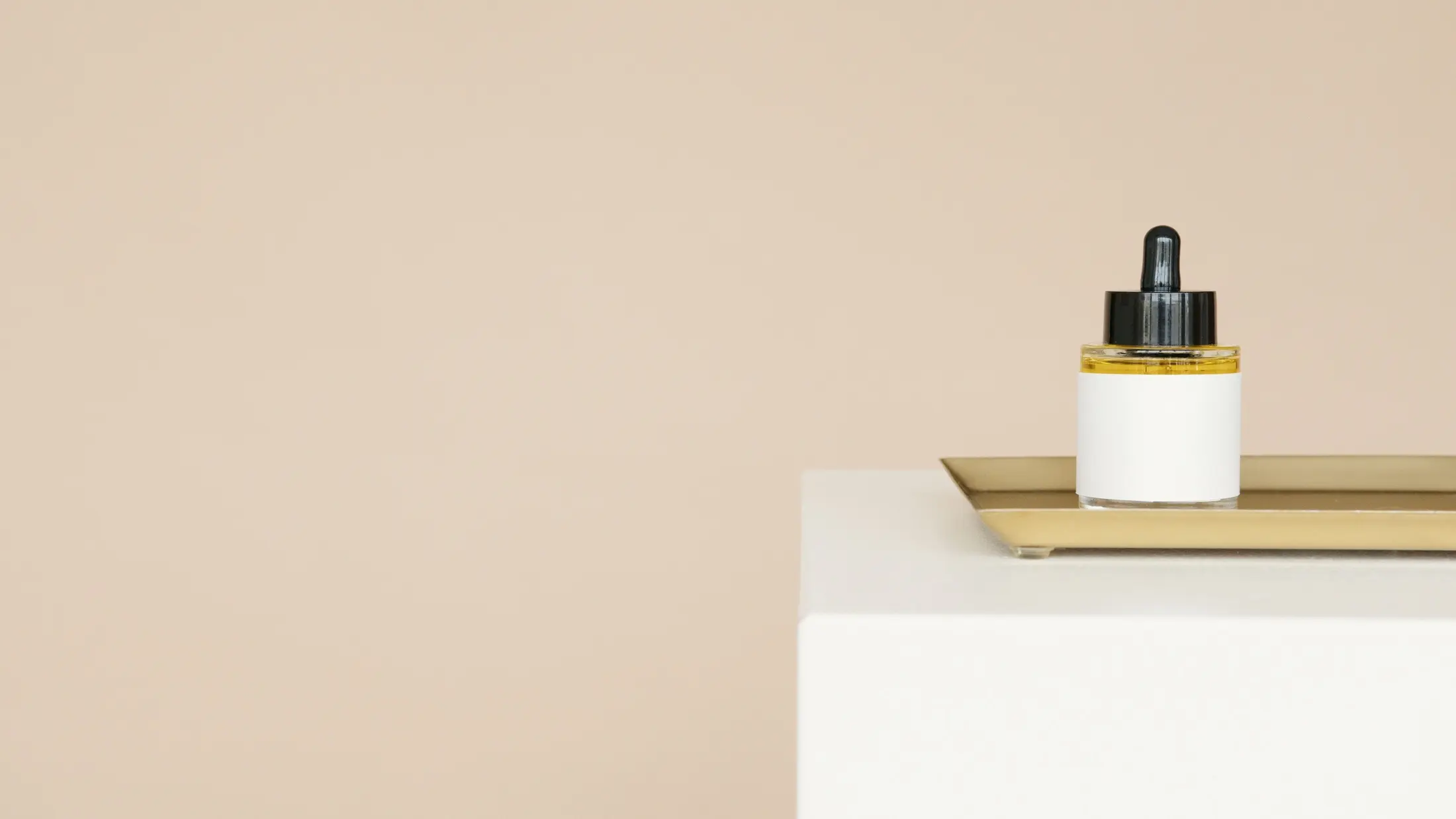 Flacon de soin posé sur un plateau doré, fond beige