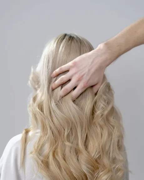 Cheveux blonds lissés vus de dos, main du coiffeur sur l'épaule